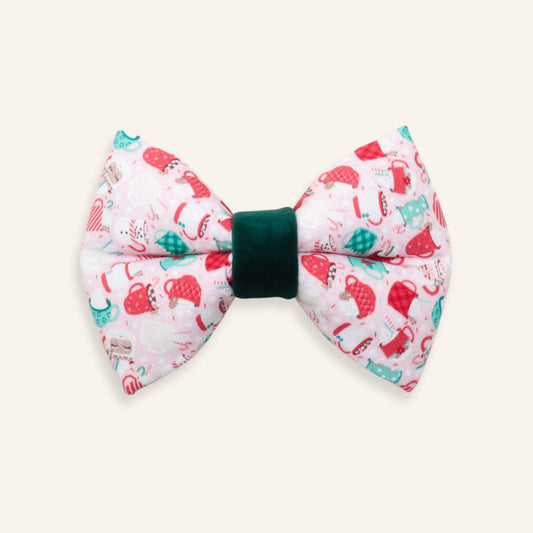 Handmade pink Christmas dog sailor bow featuring festive mugs, mittens, Santa hats, candy canes, and holiday icons with a deep green velvet center, designed to slide onto a dog collar.