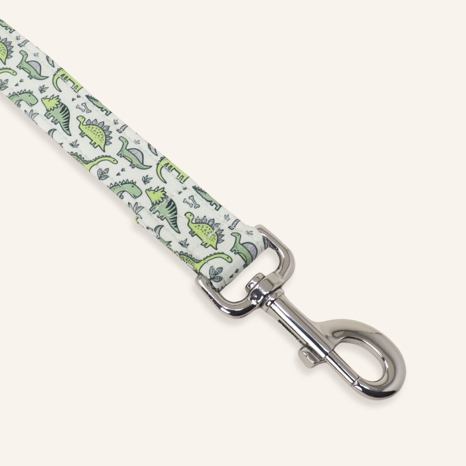 A close-up of a pet leash strap featuring a green dinosaur pattern on a white background, finished with a polished silver metal swivel clasp.