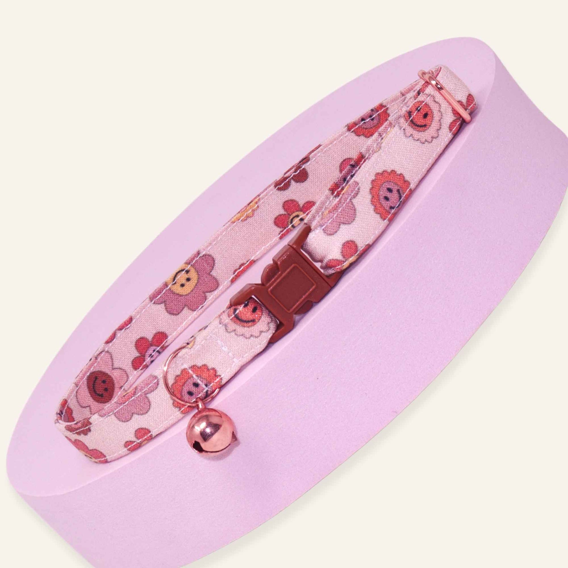 Pink breakaway cat collar featuring retro smiley flowers in blush, coral, and terracotta tones with rose gold bell.