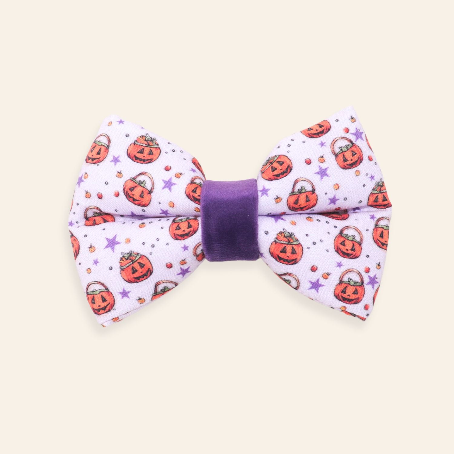 A novelty pet bow tie featuring a light purple fabric printed with orange jack-o'-lanterns, purple stars, and small candy motifs, finished with a solid purple velvet center band.