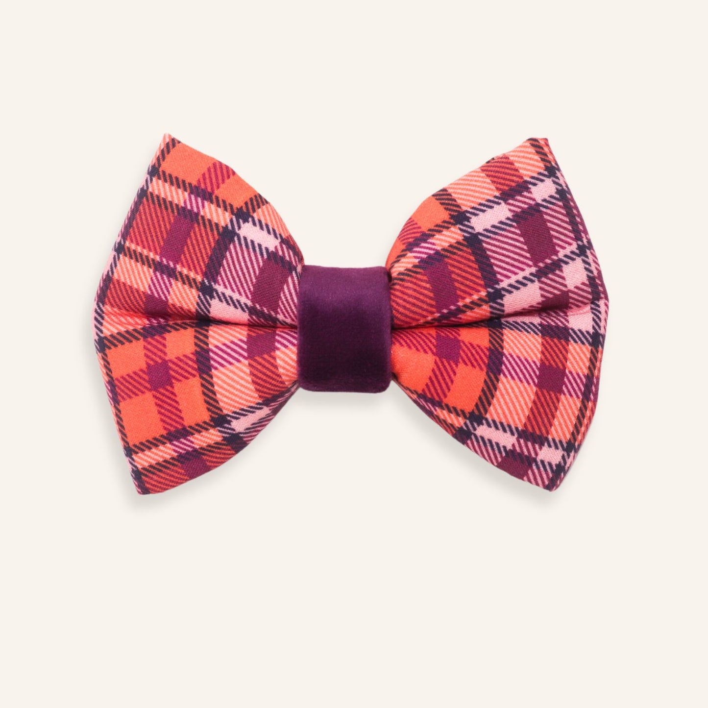 A classic pre-tied bow tie featuring a vibrant orange, pink, and red plaid pattern with a contrasting deep purple velvet center band, shown on a light cream background.