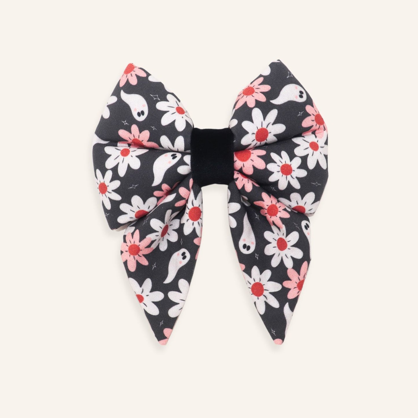 A large fabric hair bow featuring a Halloween-themed pattern of white and pink flowers with small white ghosts on a dark gray background, finished with a solid black elastic center band, shown flat on a light cream background.