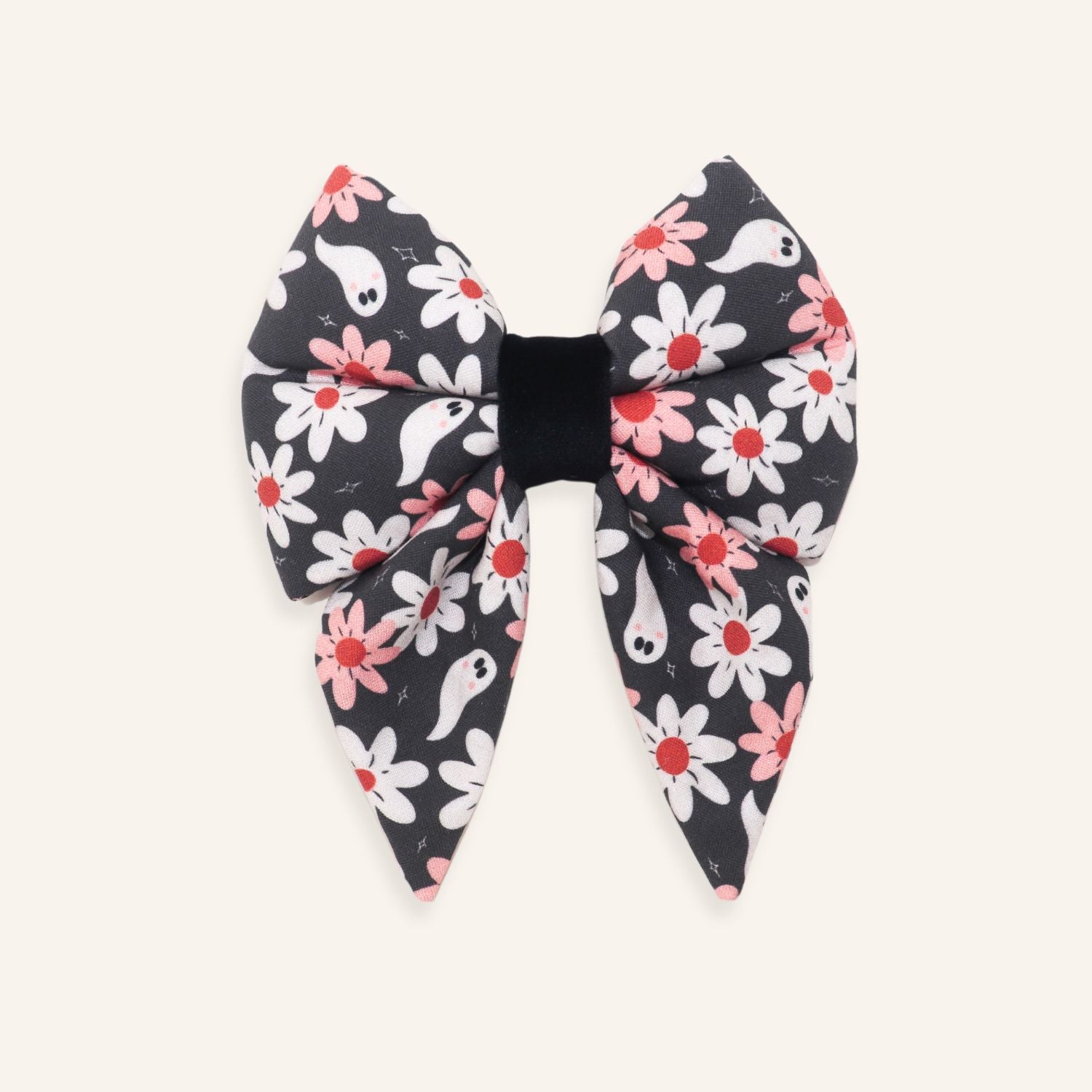 A large fabric hair bow featuring a Halloween-themed pattern of white and pink flowers with small white ghosts on a dark gray background, finished with a solid black elastic center band, shown flat on a light cream background.