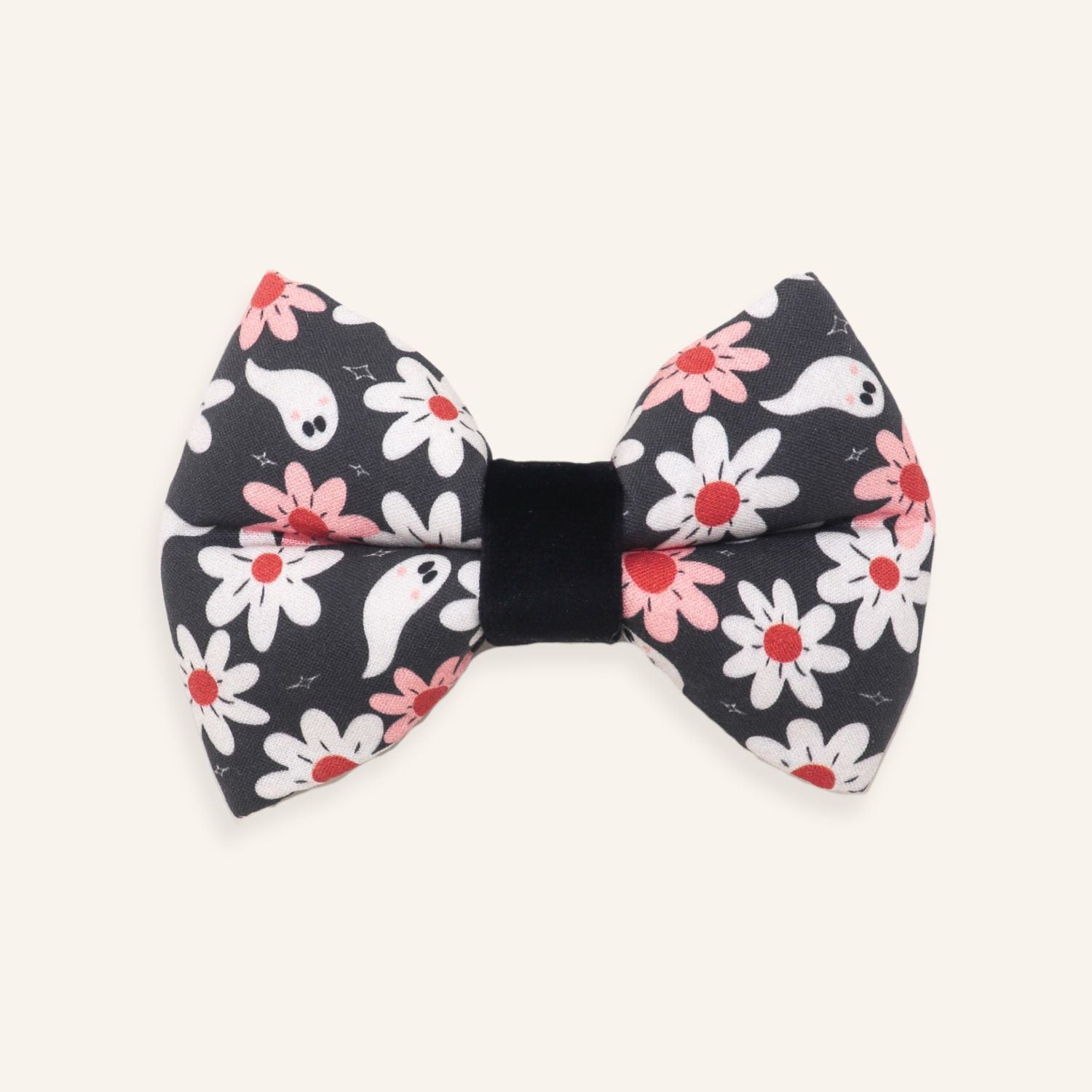 A black fabric bow tie featuring a cute Halloween pattern of white ghosts, white daisies with red centers, and pink daisies, set against a solid off-white background.