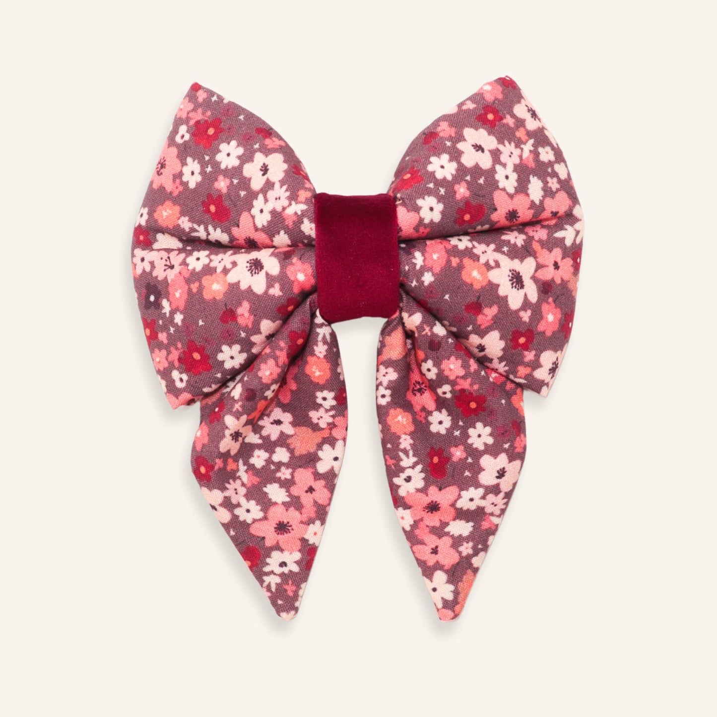 A large bow hair accessory featuring a pink, red, and white floral patterned fabric with a contrasting deep burgundy velvet center band, shown on a light cream background.