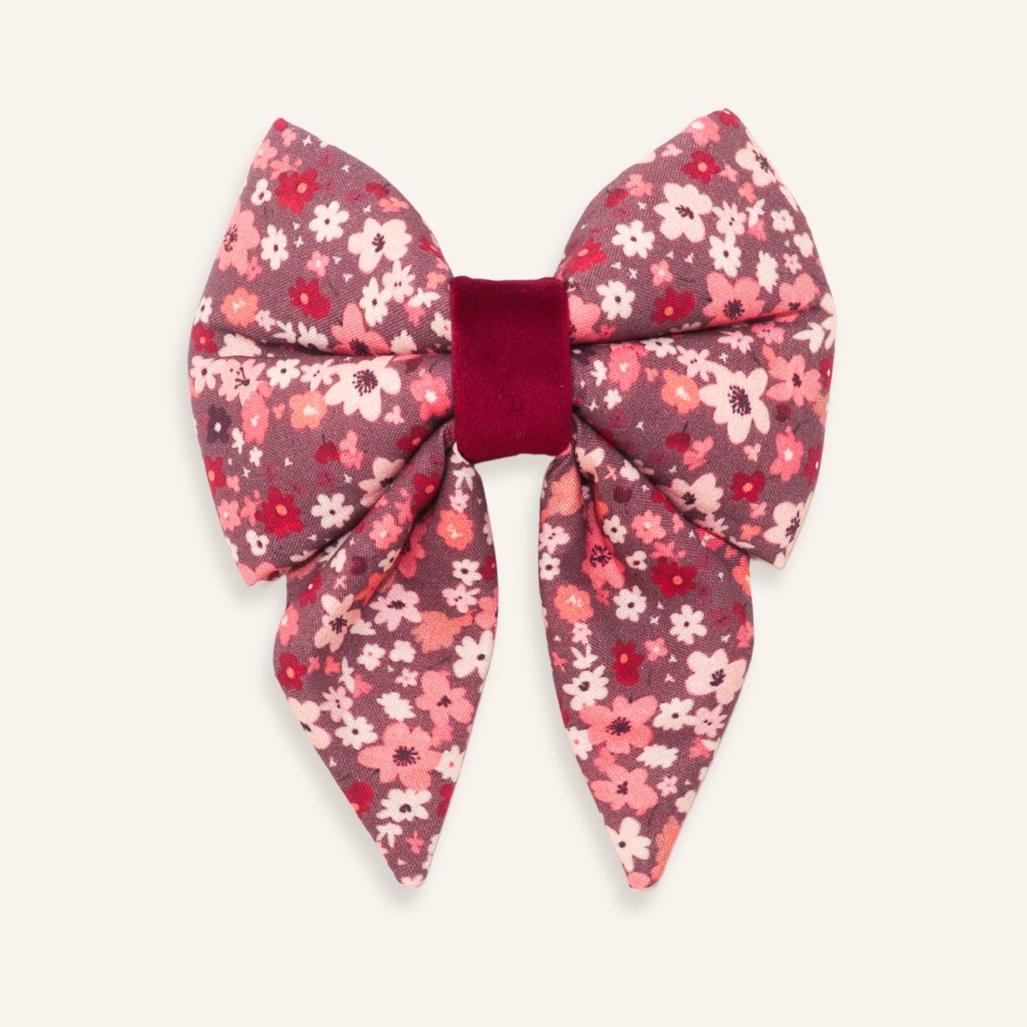 A large bow hair accessory featuring a pink, red, and white floral patterned fabric with a contrasting deep burgundy velvet center band, shown on a light cream background.