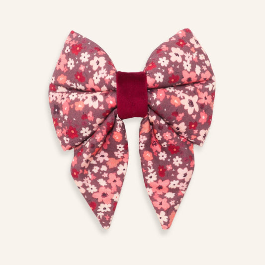 A large bow hair accessory featuring a pink, red, and white floral patterned fabric with a contrasting deep burgundy velvet center band, shown on a light cream background.