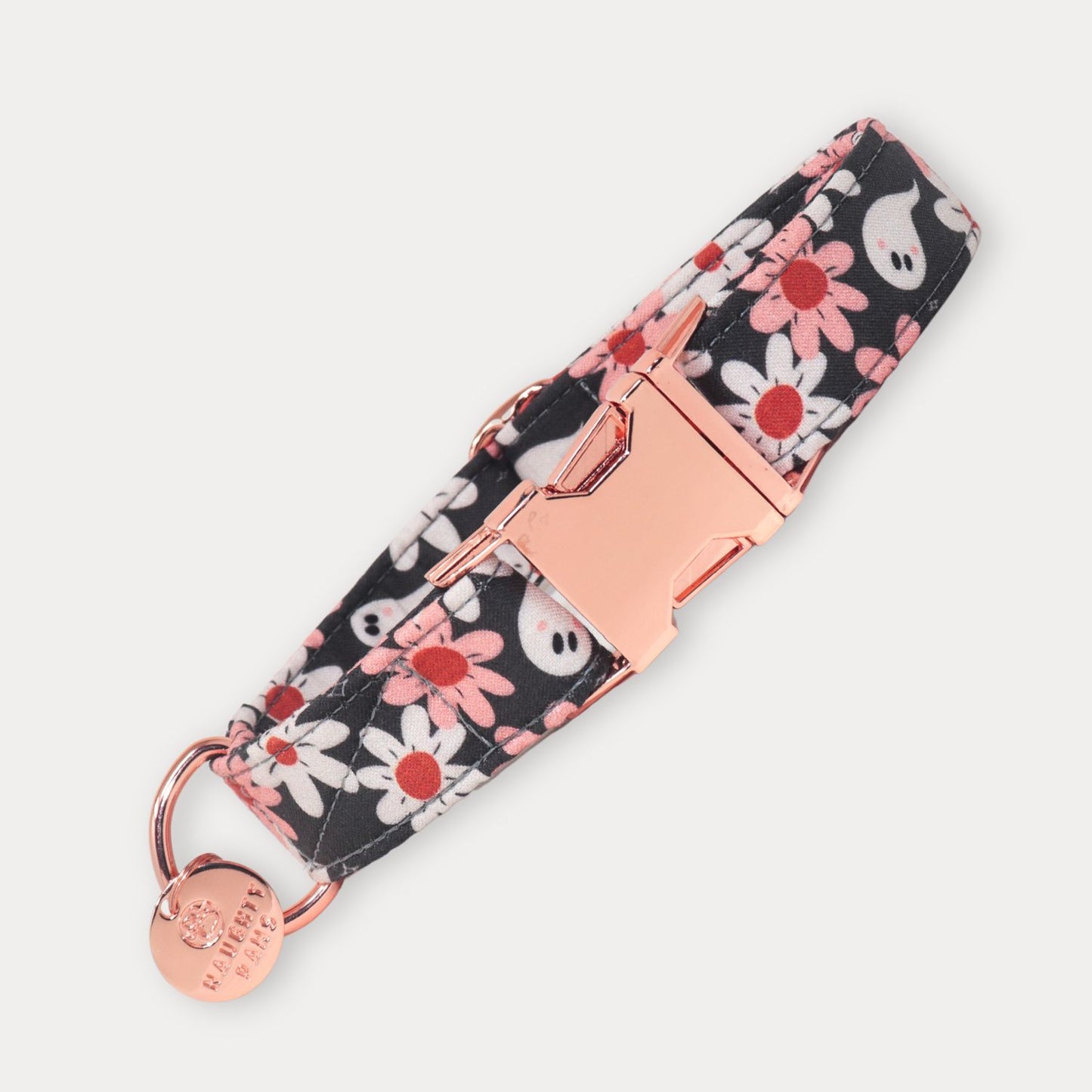 A fabric pet collar with a black background, white and pink daisy pattern, and white ghost motifs, featuring a rose gold buckle and a matching round metal tag engraved 