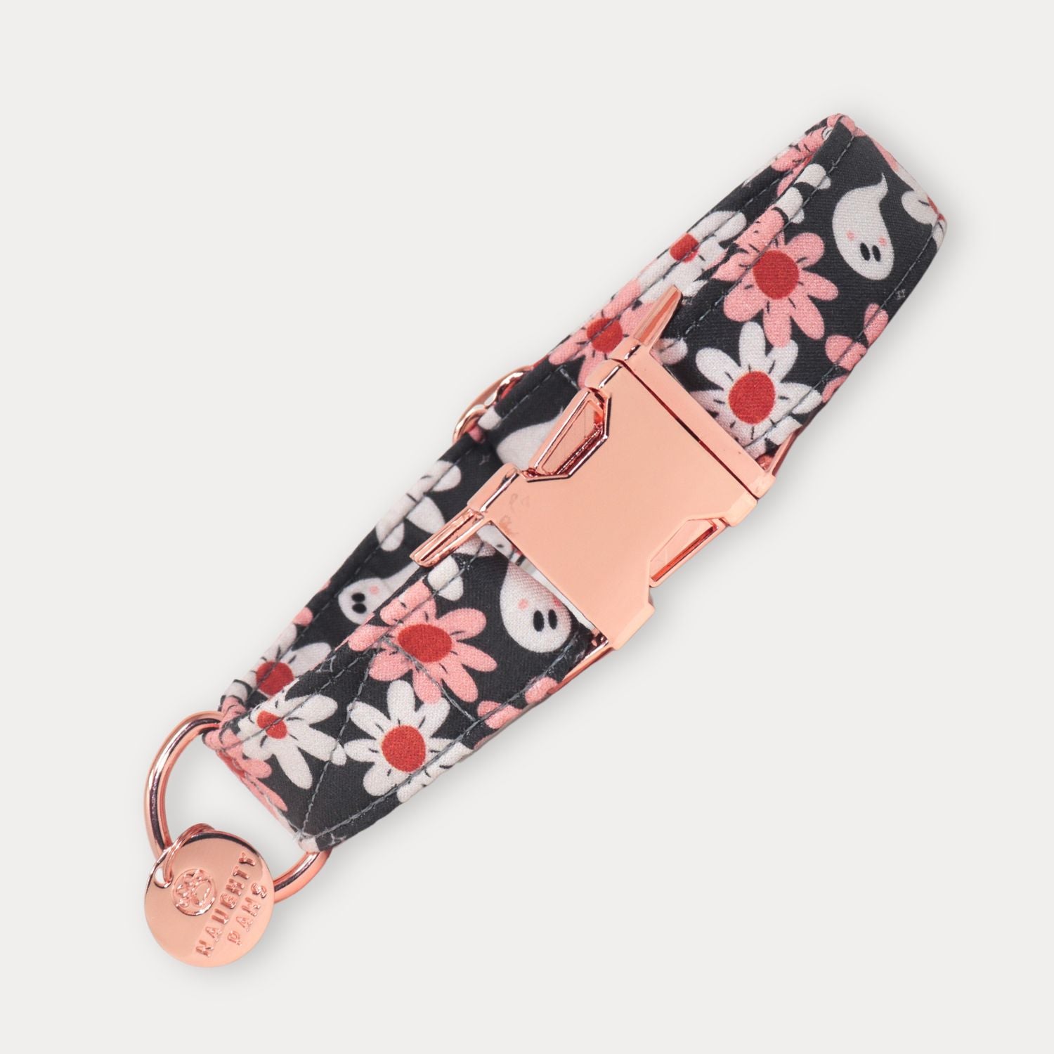 A fabric pet collar with a black background, white and pink daisy pattern, and white ghost motifs, featuring a rose gold buckle and a matching round metal tag engraved 